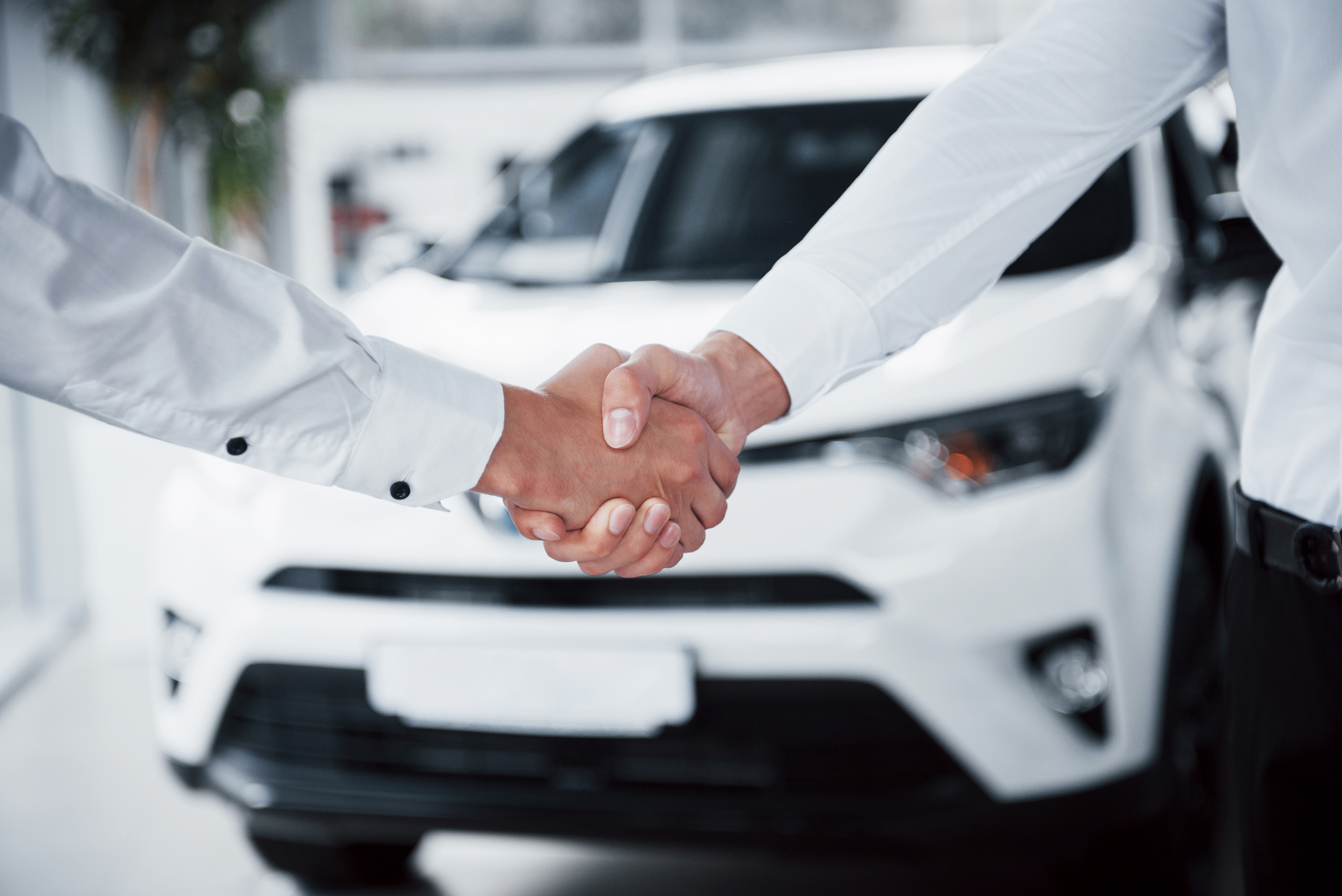 mãos de dois homens brancos se apertam em simbolo de fechar negócio de venda de carro
