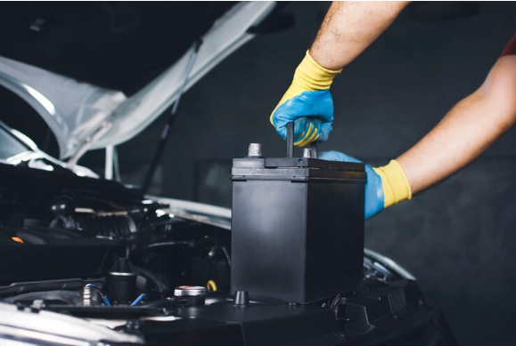 Mãos de um mecânico usando luvas manuseando a bateria de um carro