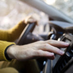 Mão de uma pessoa branca manuseando o ar condicionado ao volante do carro