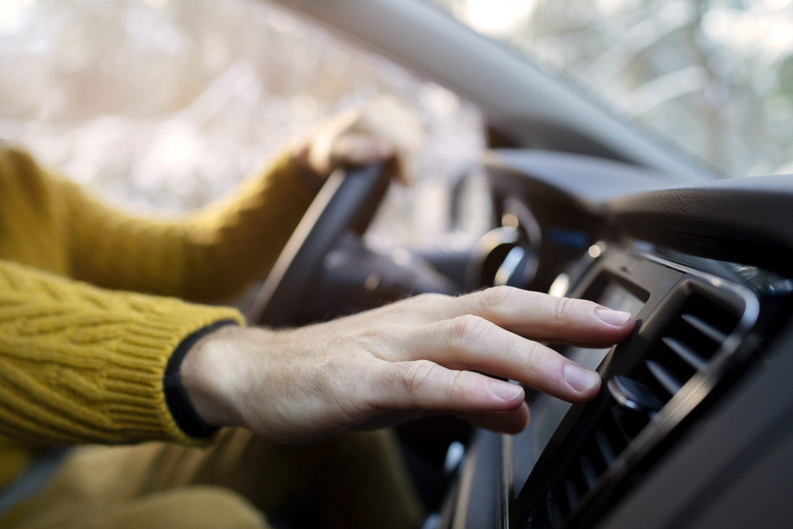 Mão de uma pessoa branca manuseando o ar condicionado ao volante do carro