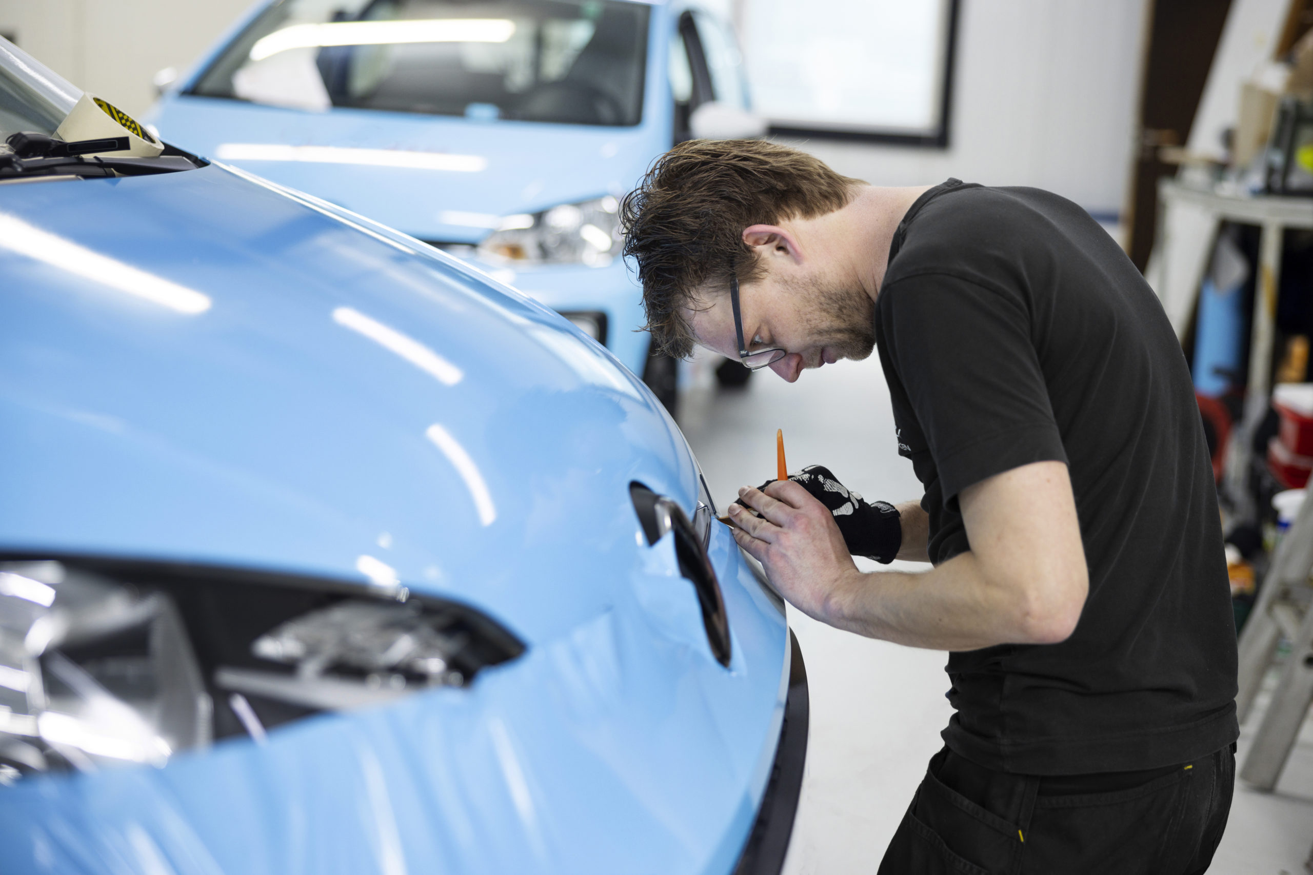 Homem branco com roupa preta envelopando um carro na cor azul claro