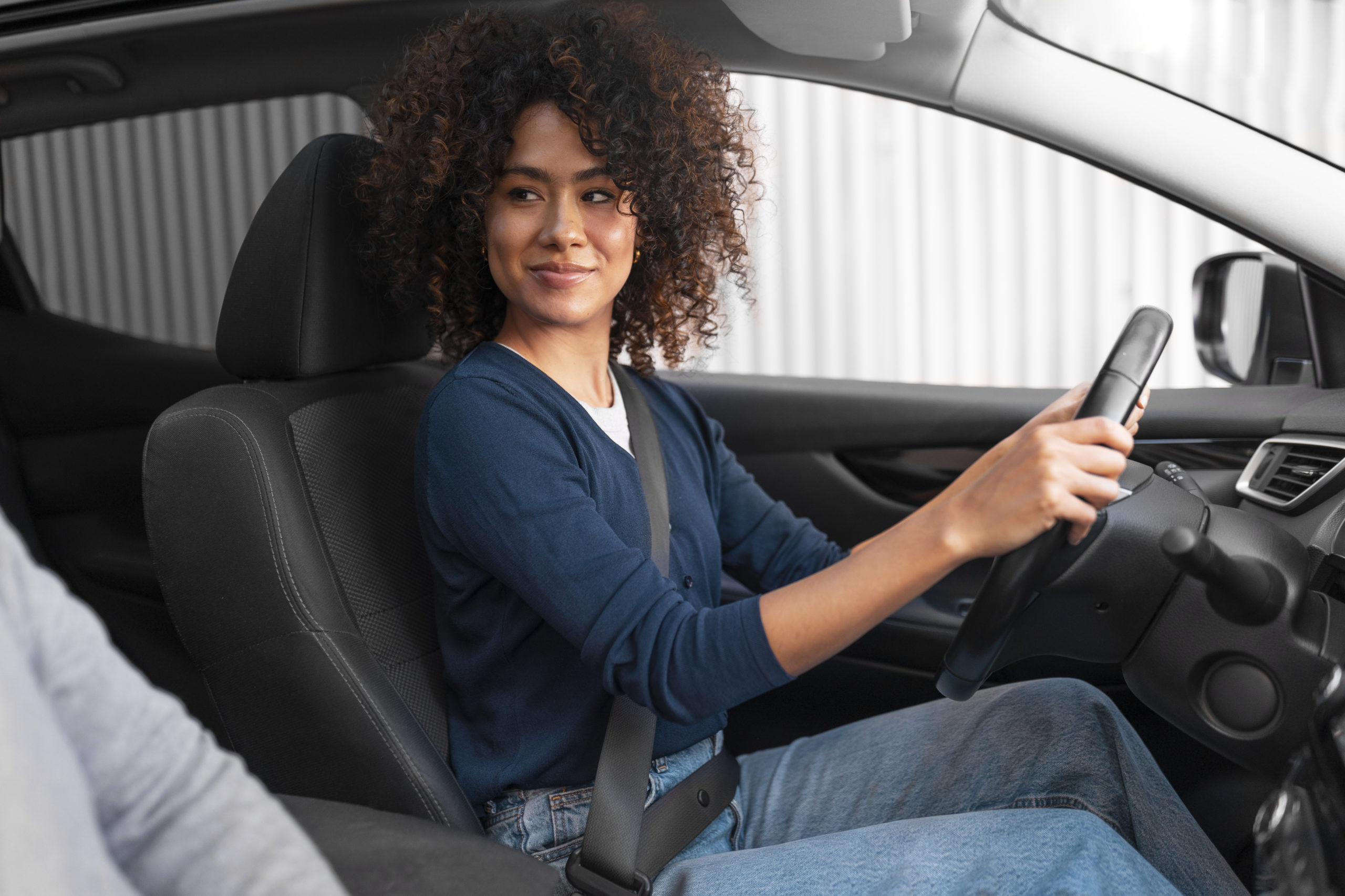 Mulher negra com blusa azul marinho e calça jeans ao volante de um carro