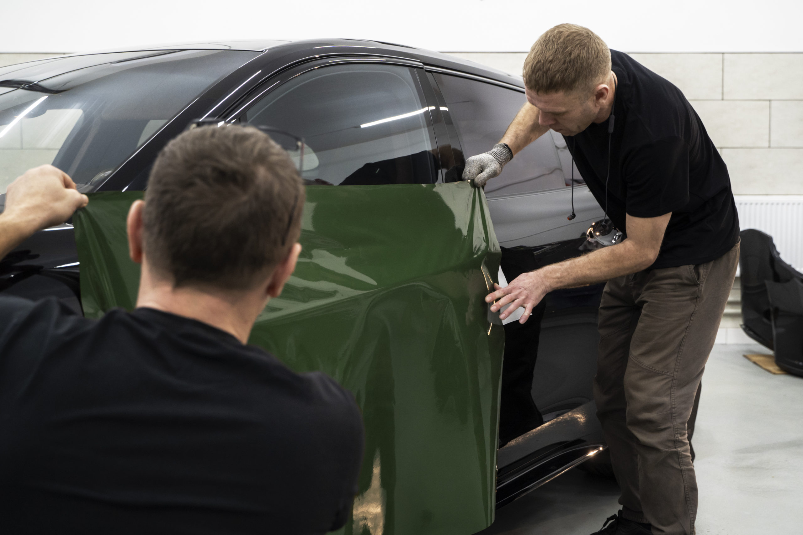 Dois homens brancos envelopando na cor verde um carro preto