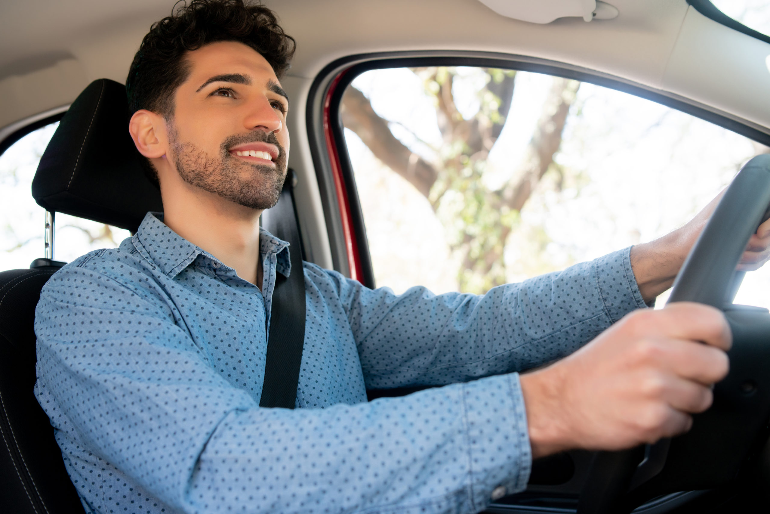 Homem branco, de camisa azul, sorrindo ao volante do carro