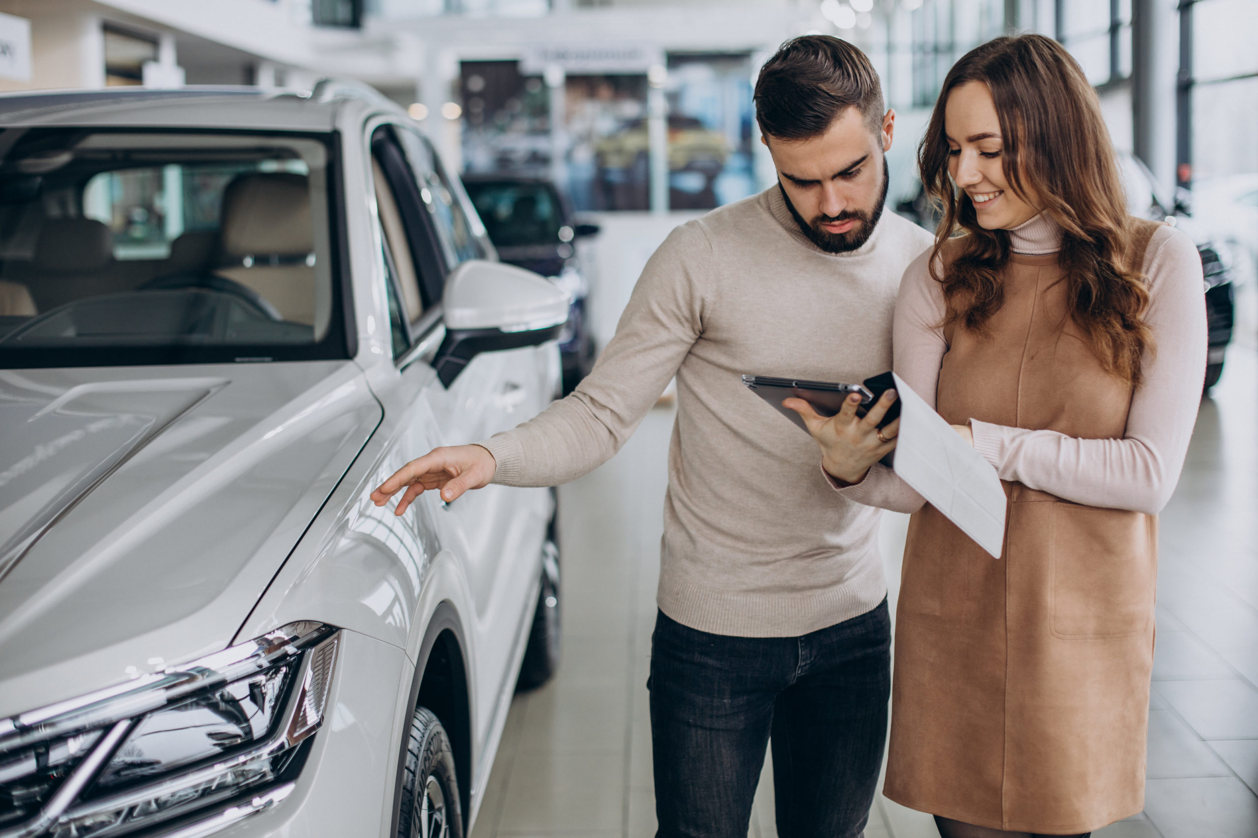 Homem e mulher brancos lendo um documento enquanto compram um carro