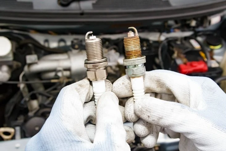 Mãos de um mecânico usando luvas brancas segurando duas velas de carro