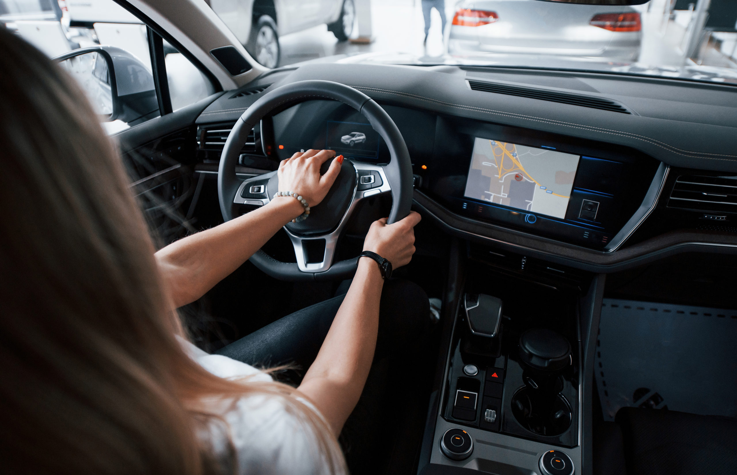 Visão de costas de uma mulher branca segurando o volante de um carro 