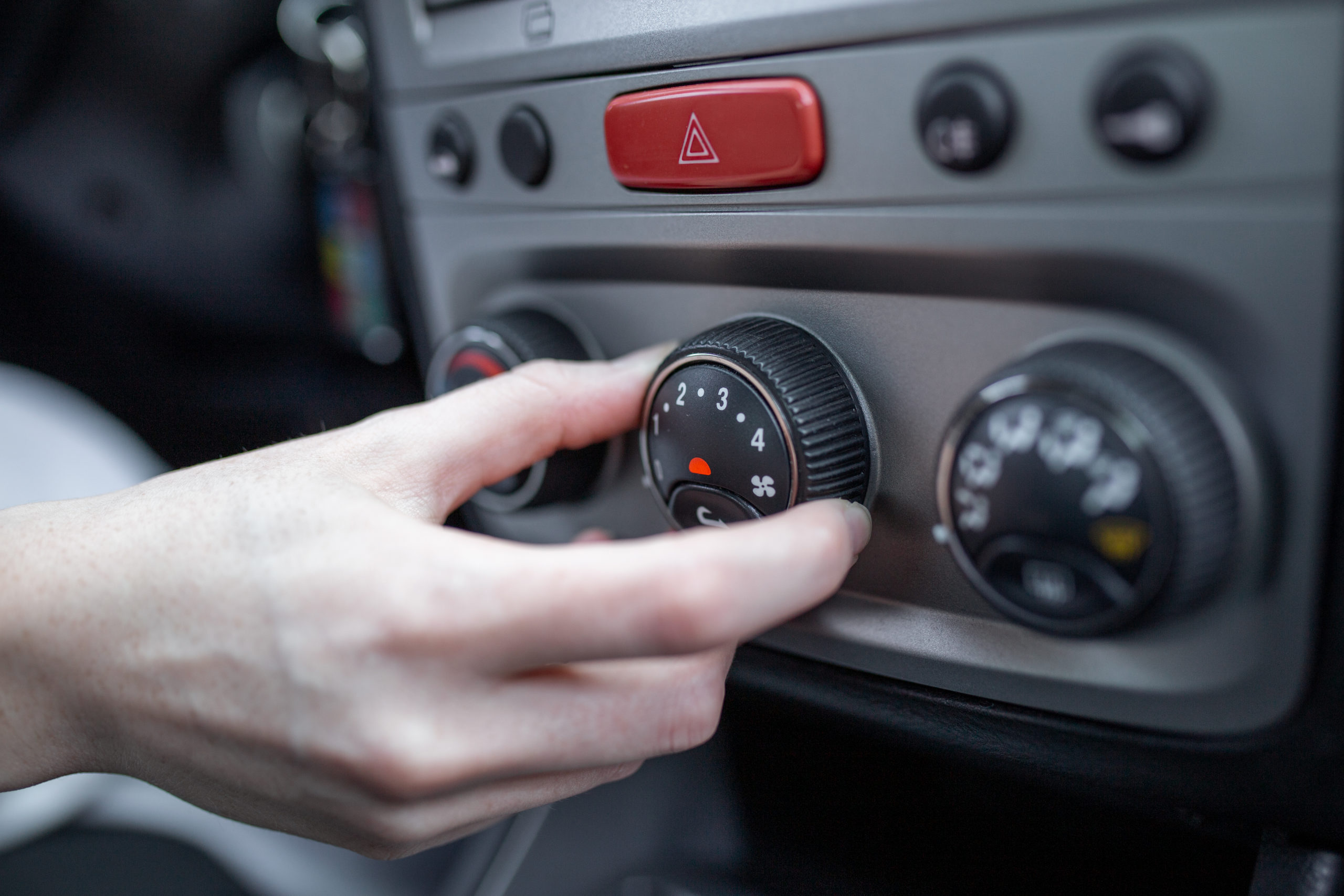 Mão de uma pessoa branca manuseando o ar condicionado ao volante do carro