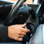 Close na mão de uma pessoa branca dando a partida na ignição do carro
