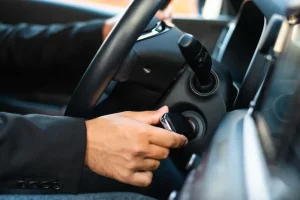 Close na mão de uma pessoa branca dando a partida na ignição do carro
