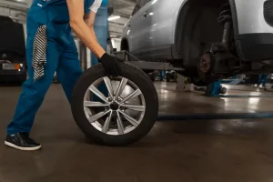 Mecânico branco com macacão azul manuseando um pneu para colocá-lo no carro