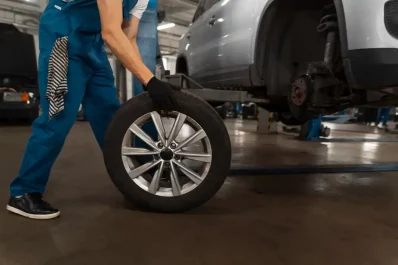 Mecânico branco com macacão azul manuseando um pneu para colocá-lo no carro