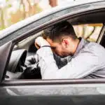 Homem branco com a cabeça encostada no volante do carro, triste