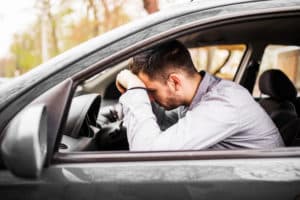 Homem branco com a cabeça encostada no volante do carro, triste