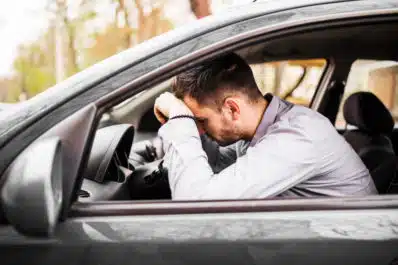 Homem branco com a cabeça encostada no volante do carro, triste