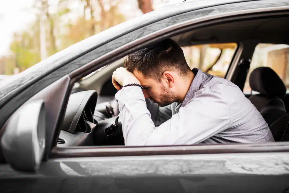 Homem branco com a cabeça encostada no volante do carro, triste