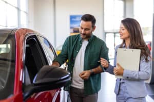 Homem branco em loja de carros com a vendedora ao lado olhando um carro vermelho