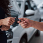 Close das mãos de pessoas brancas, uma passando a chave de um carro para a outra