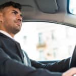Homem branco dirigindo carro vestindo terno
