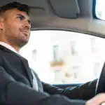 Homem branco dirigindo carro vestindo terno