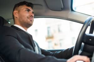 Homem branco dirigindo carro vestindo terno