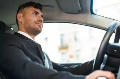 Homem branco dirigindo carro vestindo terno