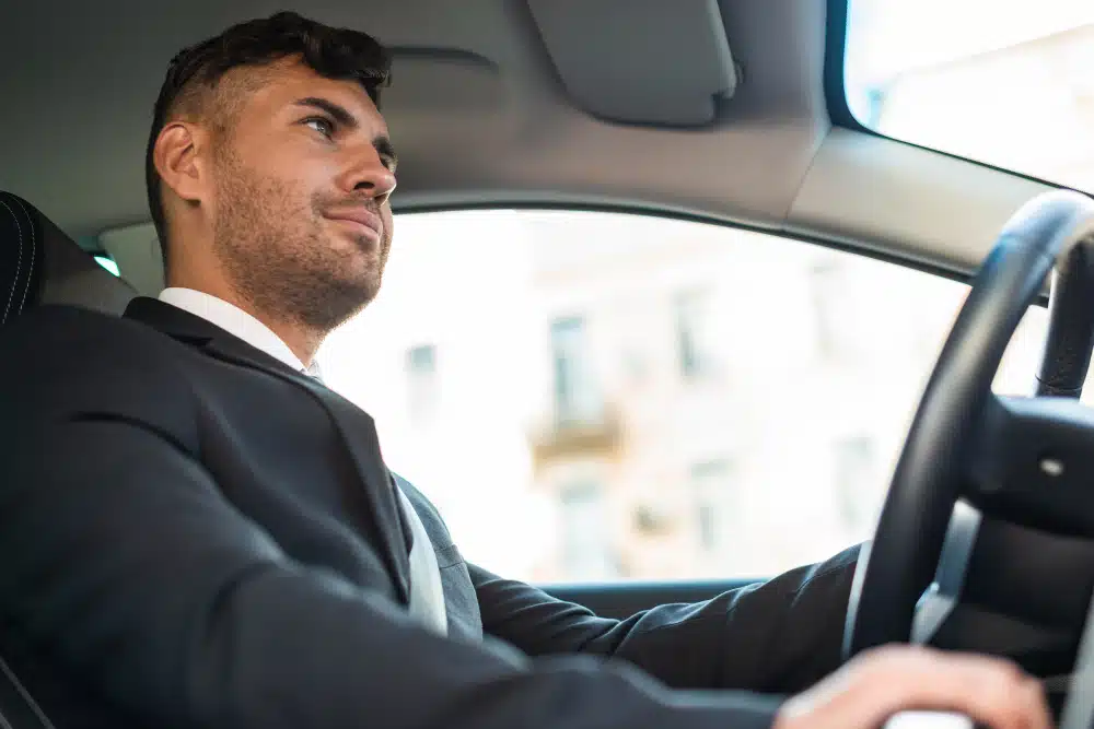 Homem branco dirigindo carro vestindo terno
