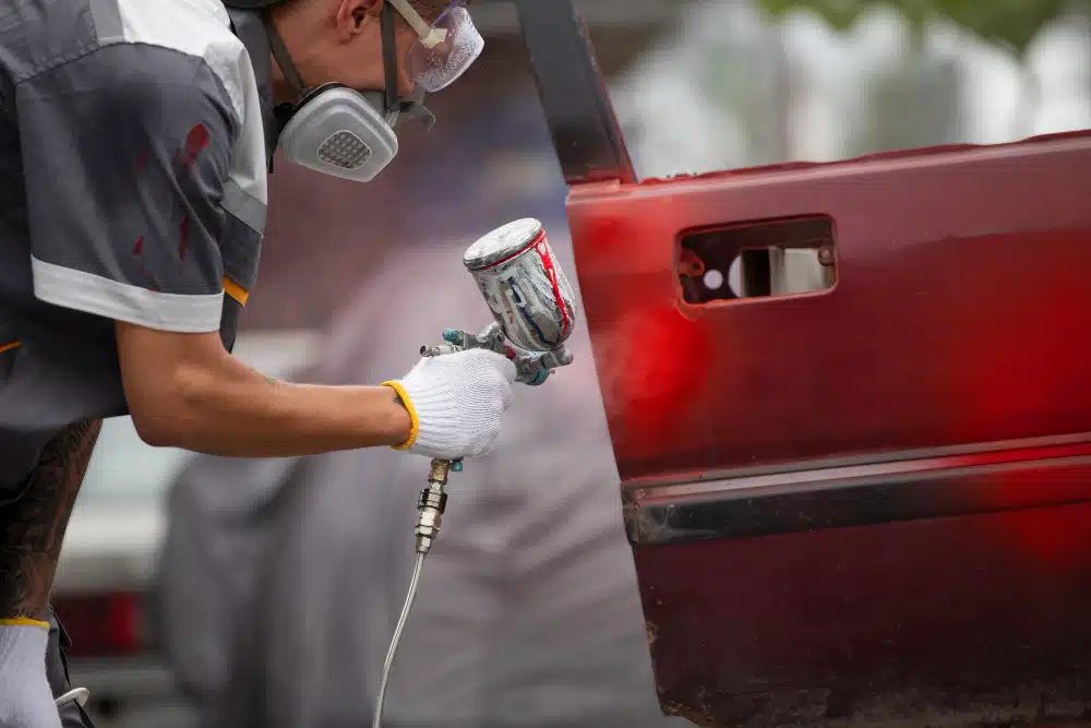Pessoa pintando um carro de vermelho com um jato de tinta